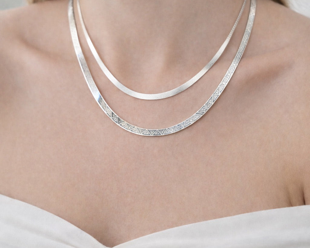 Modelo usando Cadena Herringbone Geometrica Reversibile de plata italiana 925. Muestra dos cadenas en cuello cada una mostrando un lado del diseño.
Línea Essenziale Di Vogel